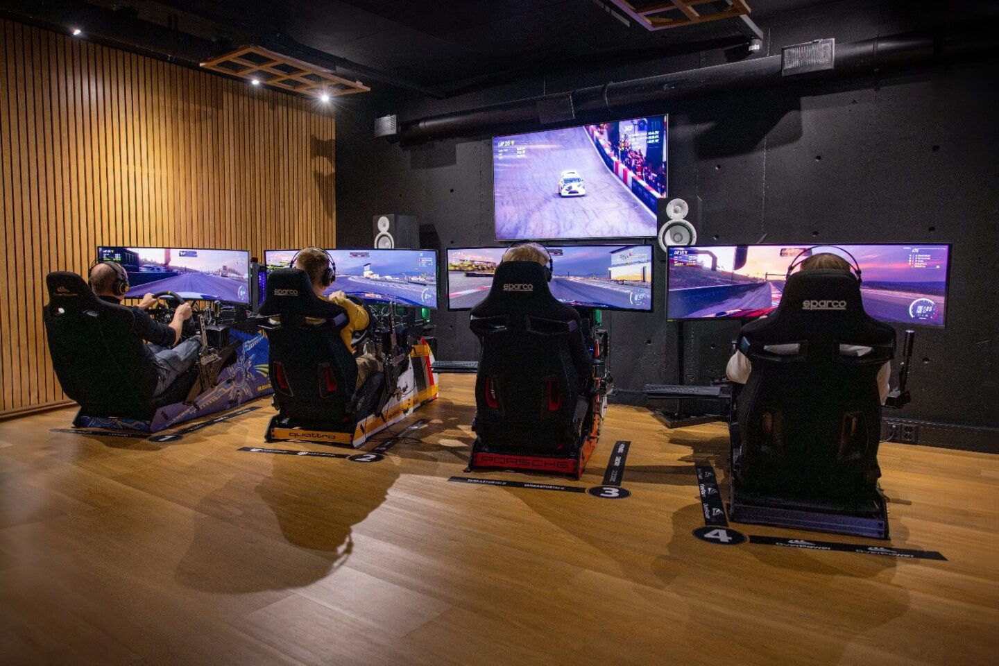 Shakedown Parkin eRally-tilan ajosimulaattorit takaapäin kuvattuna ja näytöistä heijastuu peli.